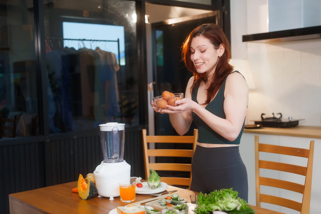 Olivia Rosewood, creator of DelishCraze, smiling as she holds a clear bowl of fresh brown eggs in her kitchen, surrounded by healthy ingredients.