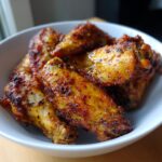 A close-up shot of golden brown, crispy Air Fryer Chicken Wings seasoned with spices, served in a white bowl.