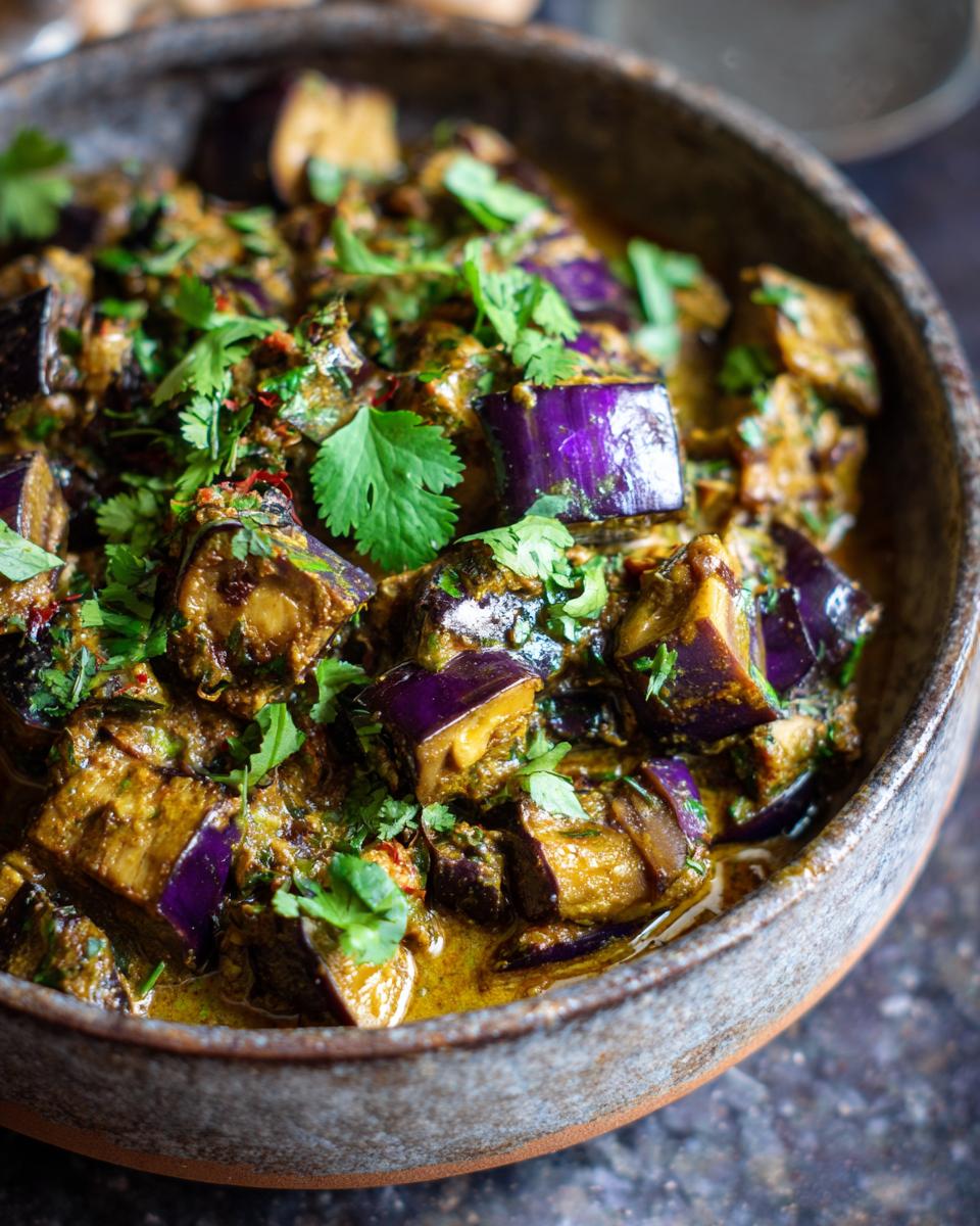 A close-up of a rustic bowl filled with creamy aubergine curry, garnished with fresh cilantro.