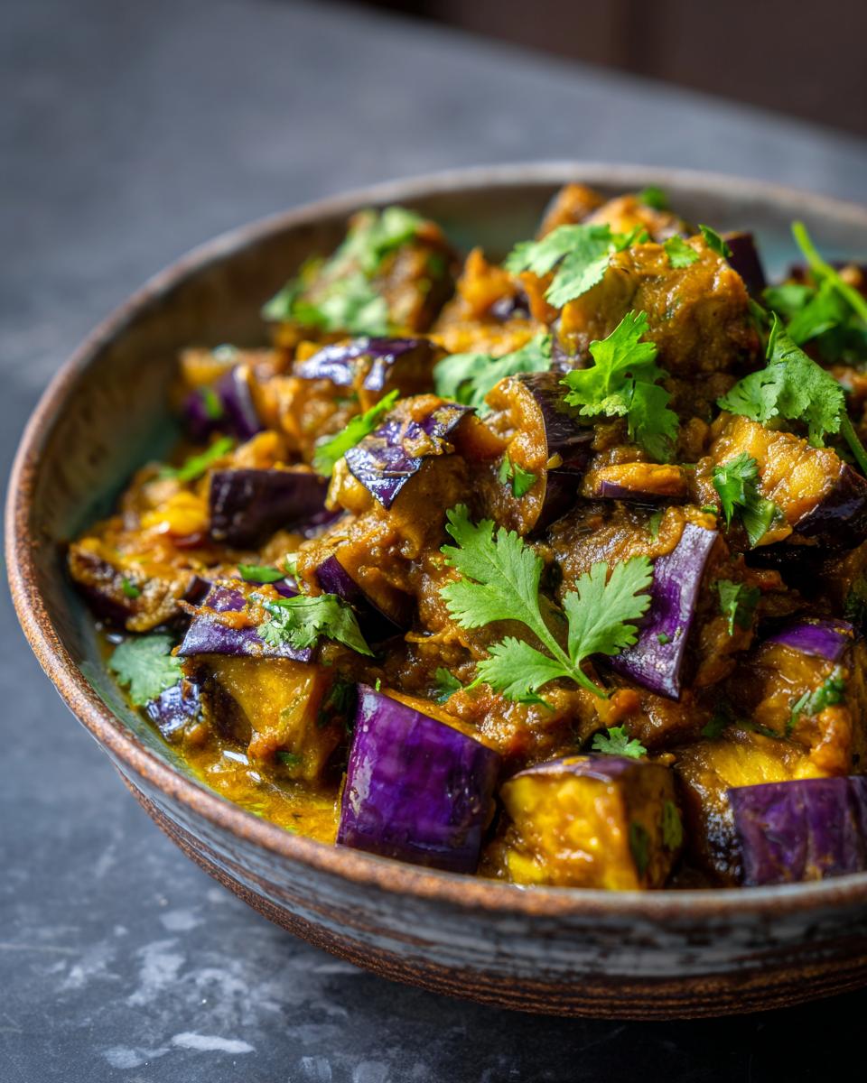 Close-up of a rustic bowl filled with creamy aubergine curry, garnished with fresh cilantro.