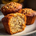 Close-up of a moist banana nut muffin, with one muffin broken open to reveal the texture and banana pieces.