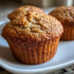 Close-up of three golden-brown banana protein muffins on a white plate.