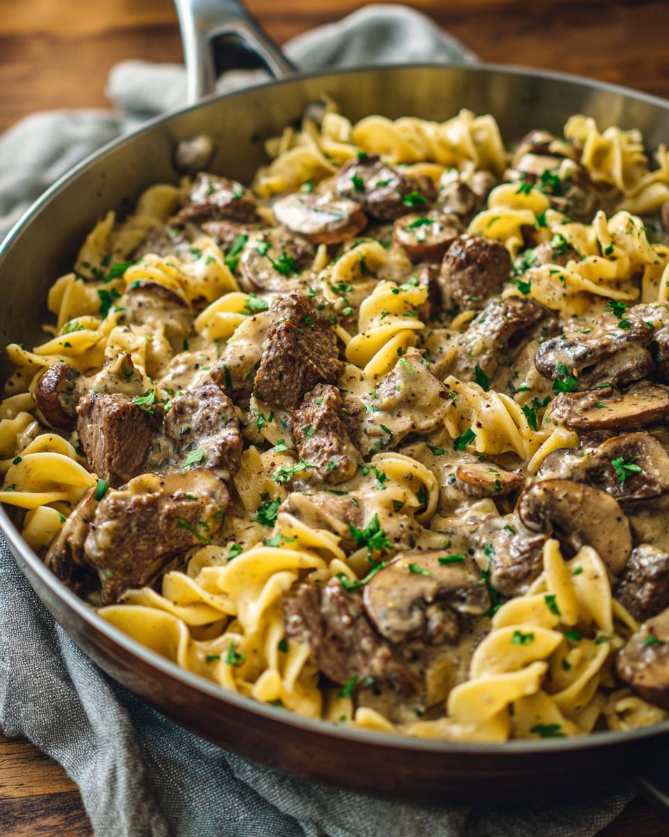 A close-up of a pan filled with creamy Beef Stroganoff, featuring tender beef, mushrooms, and egg noodles, garnished with parsley.