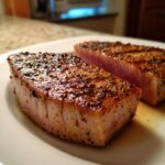 Two perfectly cooked Blackened Tuna Steak fillets on a white plate, showcasing a beautiful sear and pink interior.