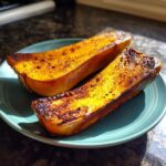 Two halves of brown sugar roasted butternut squash on a teal plate, showing caramelized edges and a vibrant orange interior.