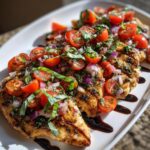 Close-up of grilled Bruschetta chicken topped with fresh cherry tomatoes, red onion, and basil, drizzled with balsamic glaze.