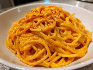 A close-up of spaghetti coated in a vibrant orange butternut squash pasta sauce, topped with red pepper flakes.