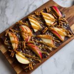 Close-up of dark chocolate caramel apple bark topped with fresh apple slices, pretzels, and caramel drizzle.