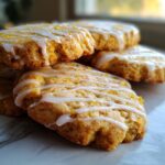 Close-up of stacked cardamom shortbread cookies with a drizzle of orange glaze and orange zest.