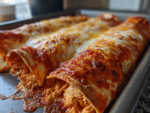Close-up of cheesy chicken enchiladas covered in red sauce and melted cheese, baked in a pan.
