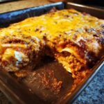 A close-up of cheesy chicken enchiladas in a baking dish, with a portion already served.