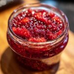 Close-up of a glass jar filled with glistening, ruby-red Christmas jam made from whole berries.