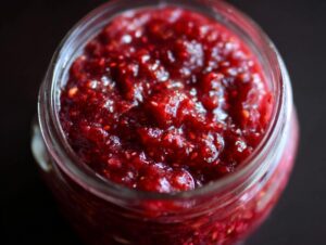 Close-up view of a jar filled with glistening, deep red Christmas jam, showcasing its chunky texture.