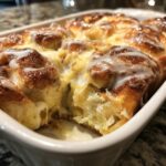 Close-up of a freshly baked cinnamon roll casserole drizzled with white glaze in a white baking dish.
