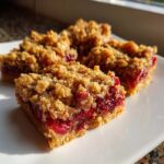 Close-up of three delicious cranberry crumble bars with a golden oat topping and a vibrant cranberry filling.