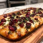 Close-up of a delicious cranberry goat cheese flatbread topped with fresh rosemary and herbs.