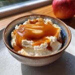 A close-up of a bowl filled with cream cheese caramel apple dip, drizzled with caramel sauce and topped with apple slices.