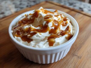 A white ramekin filled with creamy cream cheese caramel apple dip, drizzled with caramel sauce.
