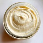 A close-up overhead view of creamy garlic aioli swirled in a glass jar, ready to be served.