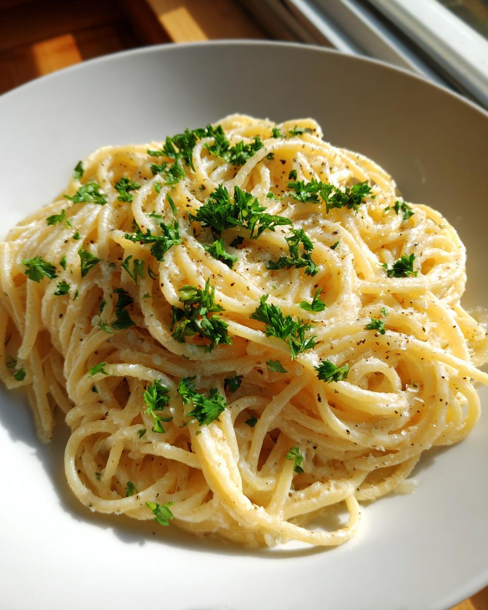 A close-up of a bowl of creamy lemon pasta, garnished with fresh parsley and black pepper.