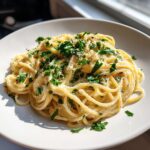 A close-up of a plate of creamy lemon pasta, garnished with fresh parsley and grated cheese.