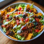 A close-up of a hearty Dorito Taco Salad with seasoned ground beef, lettuce, tomatoes, olives, cheese, and creamy dressing.