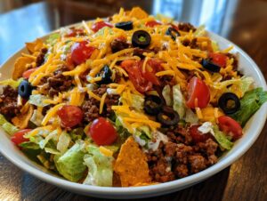 A close-up of a large bowl of Dorito Taco Salad, featuring seasoned ground beef, shredded lettuce, tomatoes, olives, and cheese.