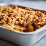 Close-up of a golden baked apple crumble in a white baking dish, showing tender apples and a crunchy topping.