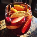 A close-up of a glass filled with fall sangria, featuring slices of orange, apple, cranberries, and cinnamon sticks.