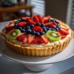 A vibrant fruit pizza sugar cookie topped with fresh strawberries, blueberries, and kiwi slices.