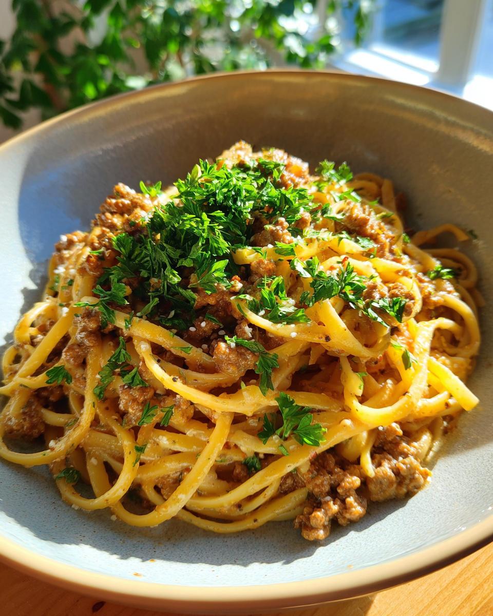 A close-up of a bowl of delicious garlic butter beef linguine, topped with fresh chopped parsley.