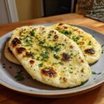 Close-up of freshly baked garlic naan bread, brushed with butter and sprinkled with chopped parsley.