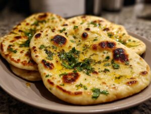 Close-up of fluffy, golden garlic naan bread topped with melted butter and fresh cilantro.