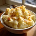 A close-up of a bowl of fluffy garlic parmesan mashed potatoes topped with crispy bits.