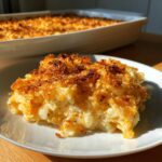 A delicious slice of golden brown hashbrown casserole on a white plate, with the rest of the casserole in the background.
