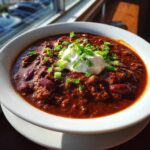 A steaming bowl of hearty 1-pot chili topped with a dollop of sour cream and fresh chopped chives.
