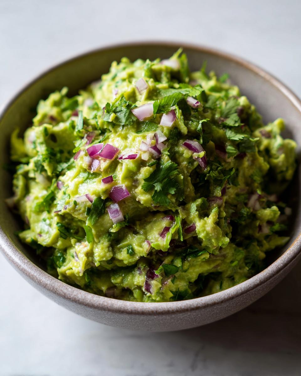A close-up of a bowl filled with fresh homemade guacamole, featuring chunky avocado, red onion, and cilantro.