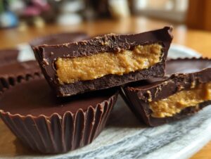 A close-up of homemade peanut butter cups, one cut in half to show the rich peanut butter filling and chocolate shell.