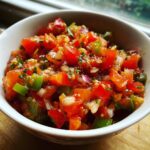 Close-up of a white bowl filled with vibrant, chunky homemade salsa, featuring tomatoes, onions, and peppers.