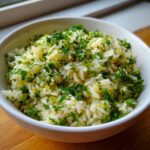 A close-up of a white bowl filled with fluffy Mediterranean lemon rice, generously garnished with fresh parsley and dill.