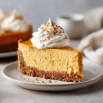 A slice of no bake pumpkin cheesecake topped with whipped cream and cinnamon on a white plate.