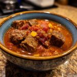 A close-up of a bowl filled with rich, red one pot Texas chili, featuring tender chunks of beef and diced tomatoes.
