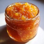 Close-up of a glass jar filled with shimmering, golden Pear Preserves.