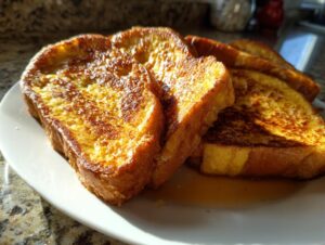 Close-up of golden-brown protein French toast slices stacked on a white plate with syrup.