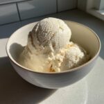 Close-up of creamy scoops of protein ice cream in a light-colored bowl, bathed in sunlight.