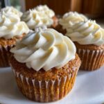 Close-up of several pumpkin spice cupcakes topped with creamy white frosting.