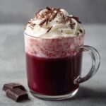 A close-up of a steaming mug of ruby hot chocolate topped with whipped cream and chocolate shavings.