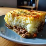 A hearty slice of Shepherd's Pie with ground beef and a fluffy mashed potato topping, garnished with herbs.