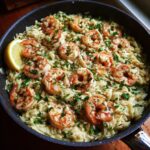 A close-up of shrimp orzo in a lemon garlic sauce, garnished with parsley and a lemon wedge.