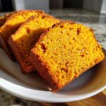 Close-up of three moist slices of sourdough pumpkin bread on a white plate, bathed in warm sunlight.